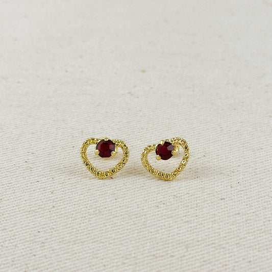 Gold heart-shaped earrings with red gemstones on a light beige background