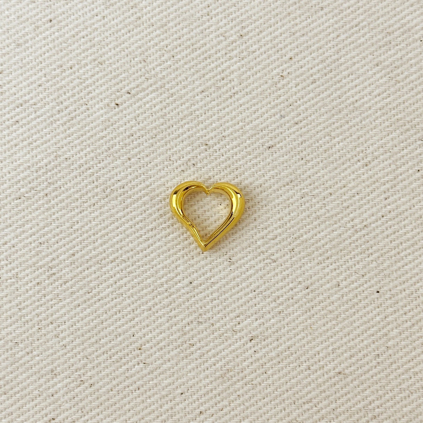 Gold heart-shaped charm on a beige fabric background